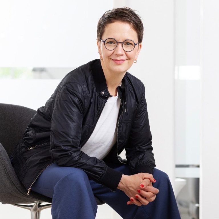 Das Bild zeigt Anika Franke, wie sie auf einem Stuhl sitzt und in die Kamera lächelt.